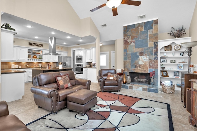 living area featuring a ceiling fan, visible vents, crown molding, and a tiled fireplace