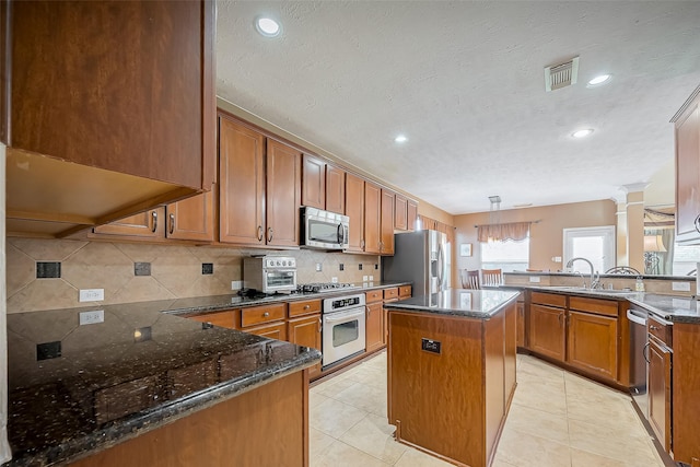 kitchen with stainless steel appliances, a peninsula, decorative backsplash, dark stone counters, and brown cabinetry