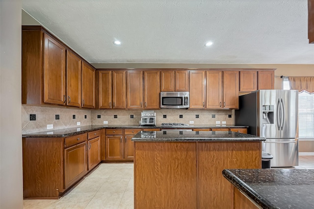 kitchen with brown cabinetry, light tile patterned floors, dark stone counters, and stainless steel appliances