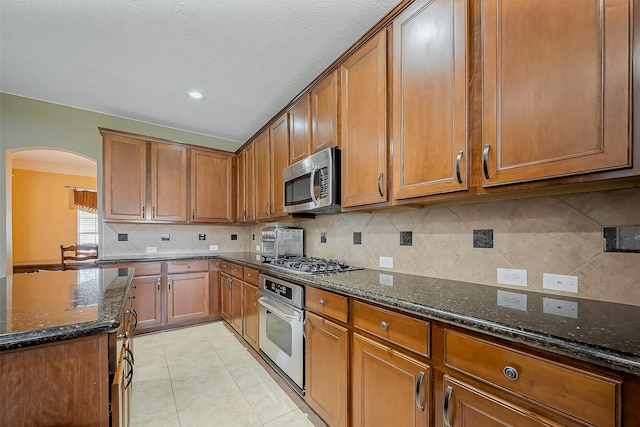 kitchen featuring appliances with stainless steel finishes, brown cabinetry, and dark stone countertops