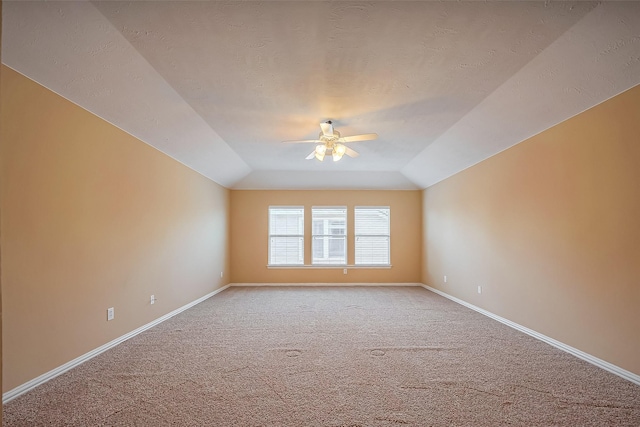 spare room featuring light colored carpet, a ceiling fan, vaulted ceiling, a textured ceiling, and baseboards