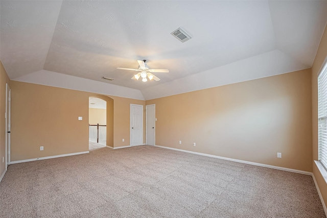 carpeted spare room featuring arched walkways, lofted ceiling, visible vents, and baseboards