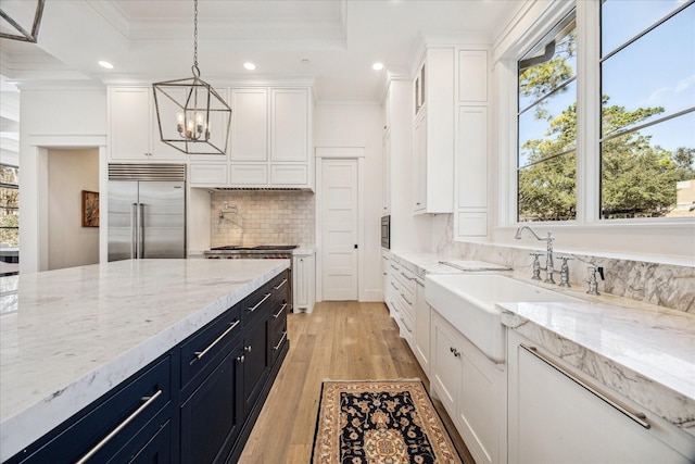 kitchen featuring ornamental molding, white cabinets, stainless steel built in fridge, a sink, and dark cabinets