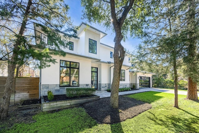 rear view of house featuring stone siding, a yard, fence, and stucco siding