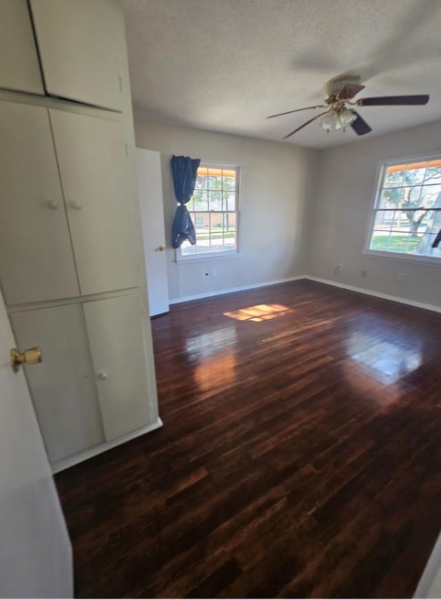 unfurnished bedroom with dark wood-type flooring, a textured ceiling, baseboards, and a ceiling fan