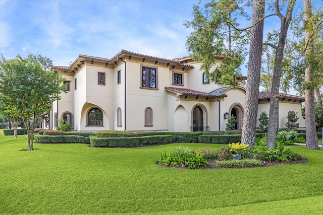 mediterranean / spanish-style house featuring a front yard, a tiled roof, and stucco siding