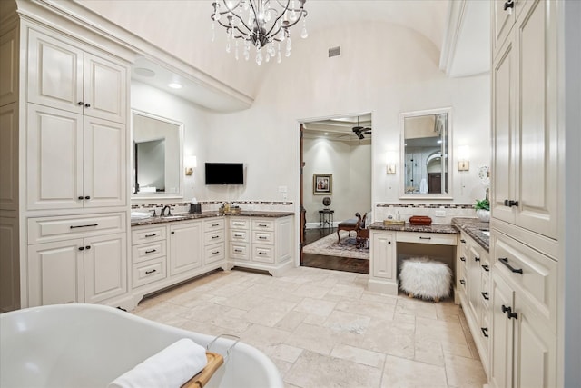 bathroom with ceiling fan with notable chandelier, tasteful backsplash, stone tile flooring, a soaking tub, and vanity