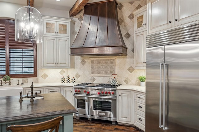 kitchen featuring premium range hood, premium appliances, glass insert cabinets, decorative light fixtures, and tasteful backsplash