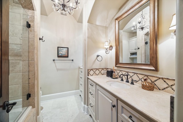 bathroom with vanity, baseboards, an inviting chandelier, a tile shower, and toilet