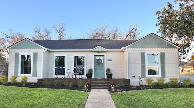 view of front of property with a front yard, covered porch, and roof with shingles