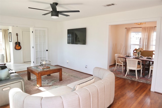 living room featuring visible vents, baseboards, wood finished floors, and a ceiling fan