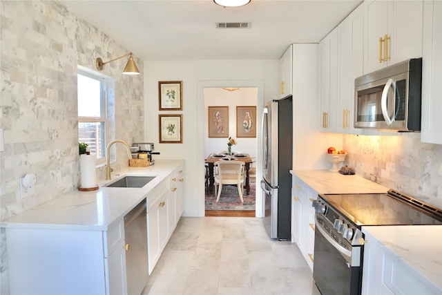 kitchen with visible vents, a sink, white cabinetry, stainless steel appliances, and light stone countertops