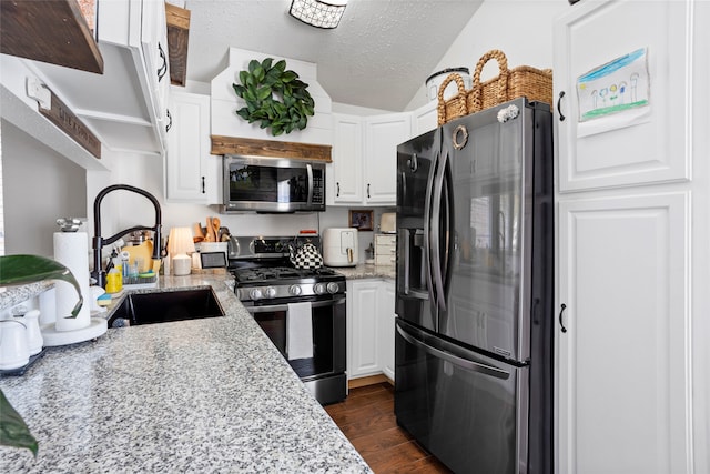 kitchen with appliances with stainless steel finishes, dark wood-type flooring, white cabinets, a sink, and a textured ceiling