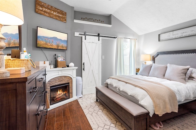 bedroom with a fireplace, lofted ceiling, a barn door, a textured ceiling, and wood finished floors