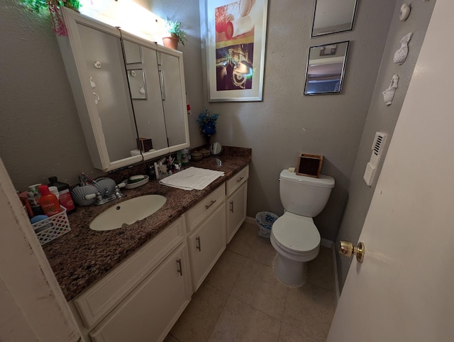 bathroom with a textured wall, toilet, vanity, baseboards, and tile patterned floors