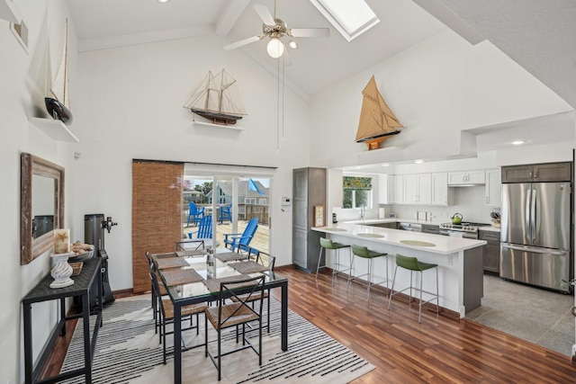 dining area with a skylight, baseboards, ceiling fan, wood finished floors, and high vaulted ceiling