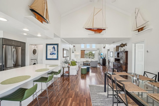 dining room featuring crown molding, dark wood finished floors, stacked washer and dryer, high vaulted ceiling, and baseboards