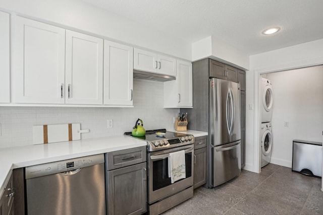 kitchen featuring under cabinet range hood, appliances with stainless steel finishes, backsplash, and stacked washer / drying machine