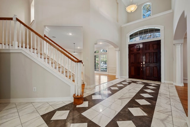 entrance foyer with ornate columns, arched walkways, baseboards, and a towering ceiling