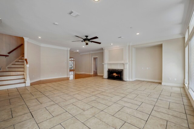 unfurnished living room featuring visible vents, ornamental molding, a ceiling fan, stairway, and a lit fireplace