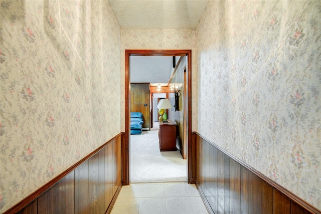 hall with a wainscoted wall, a textured ceiling, light tile patterned flooring, and wallpapered walls