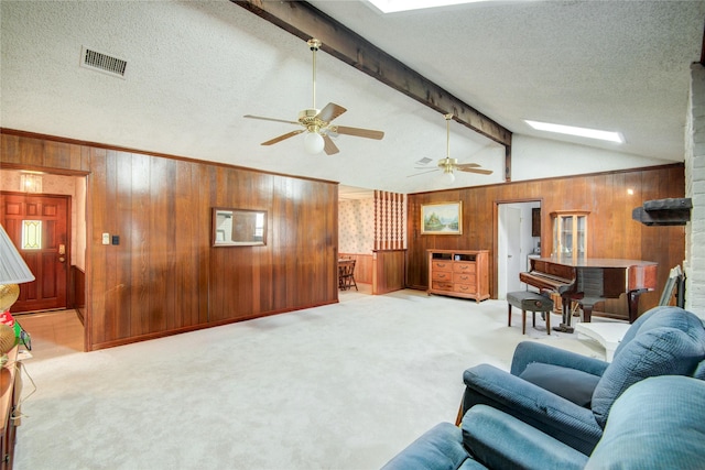 living area with visible vents, lofted ceiling with skylight, light carpet, wood walls, and a textured ceiling