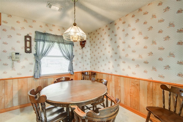 dining area featuring a textured ceiling, wood walls, visible vents, wainscoting, and wallpapered walls