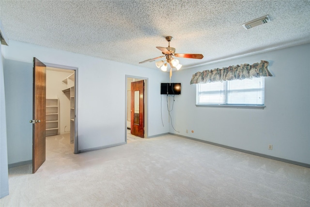 unfurnished bedroom featuring carpet floors, visible vents, a walk in closet, and a textured ceiling