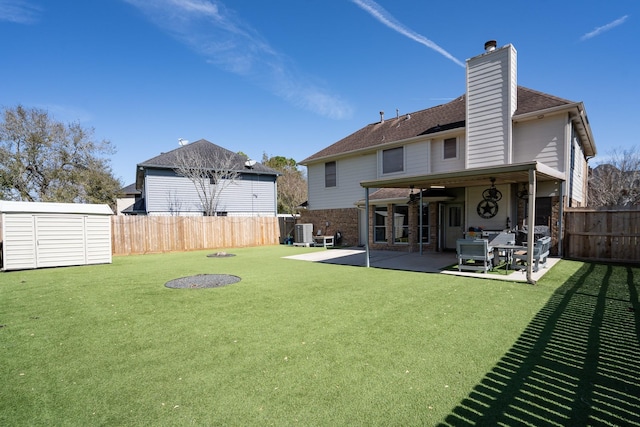 rear view of property with a patio, a fenced backyard, an outbuilding, a storage unit, and a yard