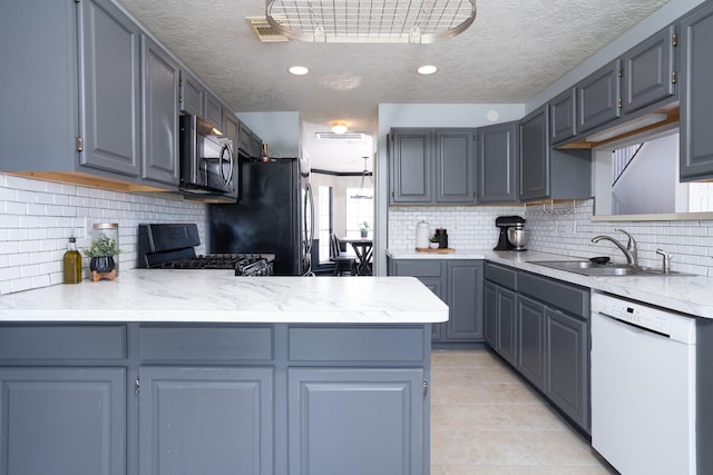 kitchen with light countertops, appliances with stainless steel finishes, a peninsula, and a sink