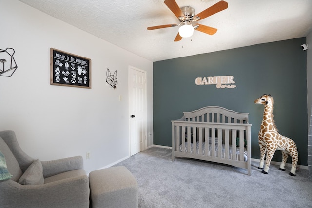 bedroom featuring a ceiling fan, carpet flooring, a textured ceiling, a nursery area, and baseboards