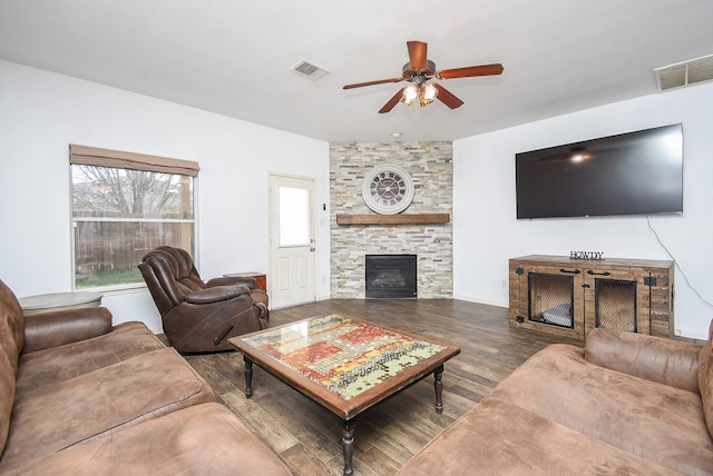 living room with visible vents, ceiling fan, a stone fireplace, and wood finished floors