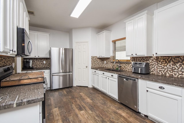 kitchen with dark wood finished floors, backsplash, appliances with stainless steel finishes, white cabinetry, and a sink