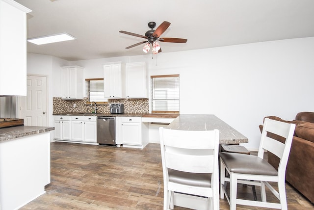 kitchen with wood finished floors, a kitchen breakfast bar, white cabinets, stainless steel dishwasher, and decorative backsplash