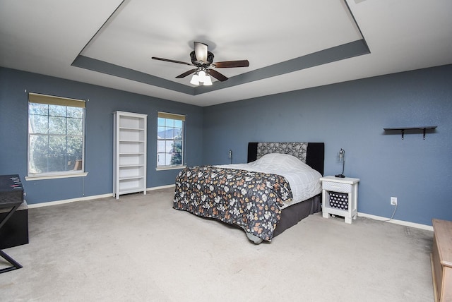 carpeted bedroom with a raised ceiling, ceiling fan, and baseboards