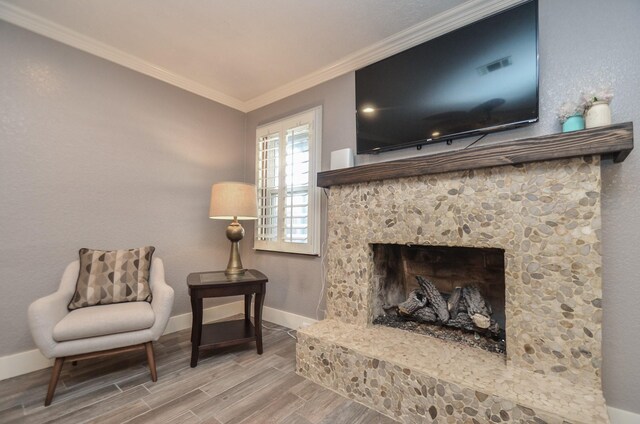 living area with wood finish floors, a stone fireplace, crown molding, and baseboards