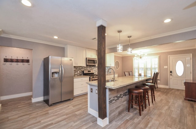 kitchen with backsplash, white cabinetry, light wood-style floors, appliances with stainless steel finishes, and a breakfast bar area