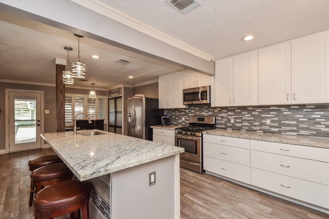 kitchen with wood finished floors, visible vents, a sink, decorative backsplash, and appliances with stainless steel finishes