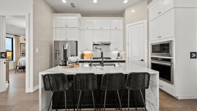 409 Silver Moon Way, Katy, TX 77493 - kitchen with stainless steel appliances, under cabinet range hood, white cabinets, a sink, and a kitchen breakfast bar