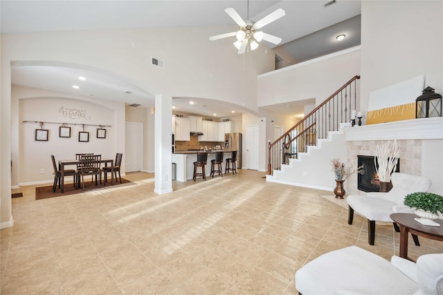 living room featuring visible vents, stairway, a tiled fireplace, ceiling fan, and baseboards