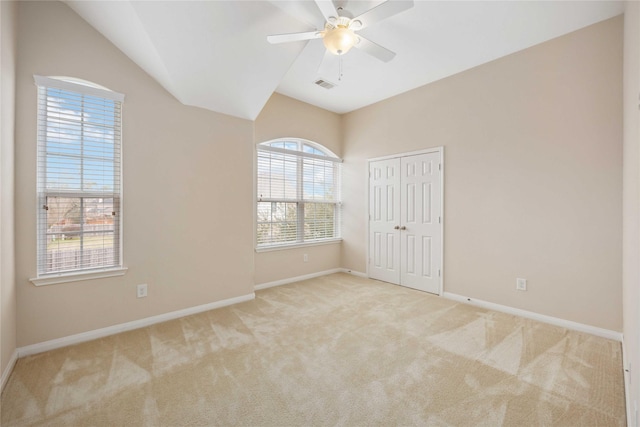 carpeted empty room featuring a ceiling fan, visible vents, vaulted ceiling, and baseboards