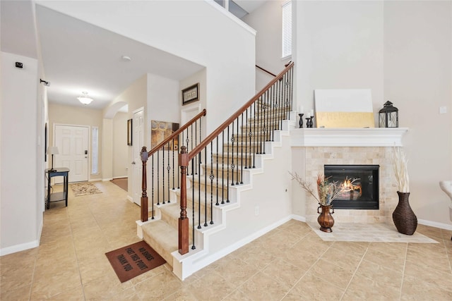 staircase with baseboards, arched walkways, a tiled fireplace, tile patterned flooring, and a high ceiling