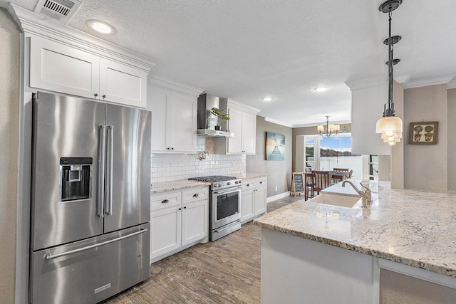 kitchen with a sink, high quality appliances, ornamental molding, and wall chimney range hood