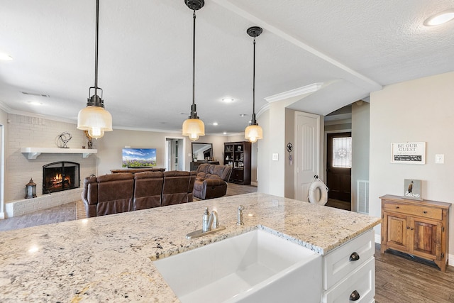 kitchen featuring visible vents, a sink, wood finished floors, light stone countertops, and a brick fireplace