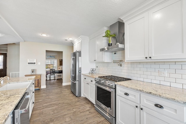 kitchen with wall chimney range hood, light wood-style flooring, white cabinets, stainless steel appliances, and a sink