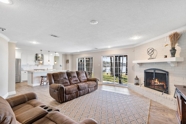 living area with visible vents, a brick fireplace, light wood-type flooring, ornamental molding, and a textured ceiling