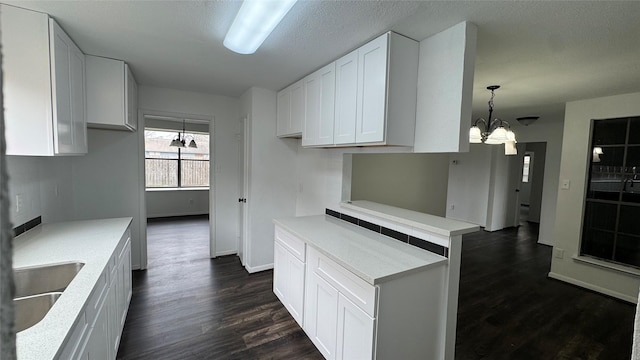 kitchen featuring white cabinets, dark wood finished floors, a sink, light countertops, and a notable chandelier