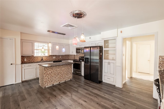 kitchen with dark stone counters, a kitchen island, dark wood-type flooring, stainless steel appliances, and backsplash