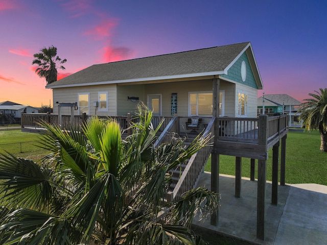 back of house featuring covered porch, a shingled roof, and a lawn