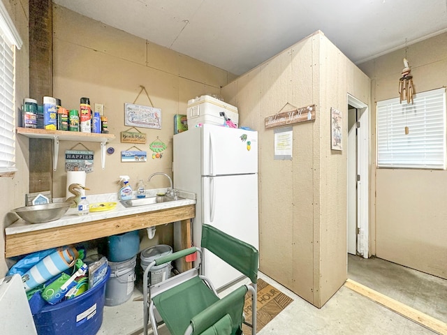 kitchen featuring freestanding refrigerator, a sink, and concrete floors